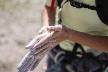 Climber with a harness and backpack rubs chalk onto his hands.