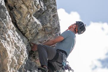 A climber on a rock face; on the right, a blue sky with thick white clouds can be seen.