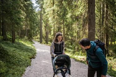 A man and a woman are walking through the forest with a stroller