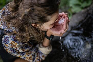 Una donna beve acqua da un ruscello