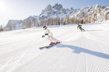 A man and a woman ski down a slope