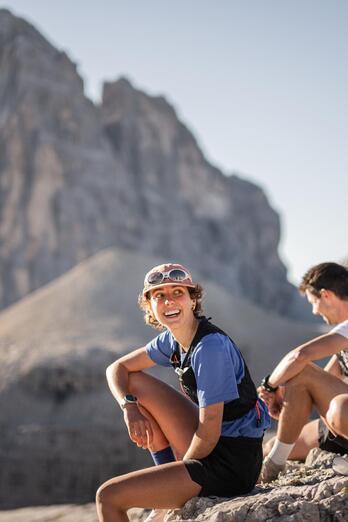Tre trail runner siedono su un terreno roccioso e osservano l’imponente paesaggio montano.