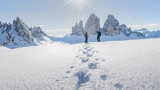 Two people look at the snow-covered Three Peaks