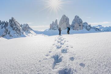Two people look at the snow-covered Three Peaks