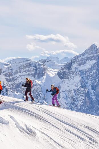 Three people are snowshoeing surrounded by the Dolomites