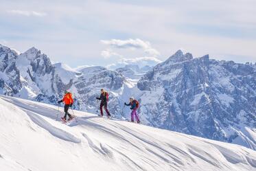 Three people are snowshoeing surrounded by the Dolomites