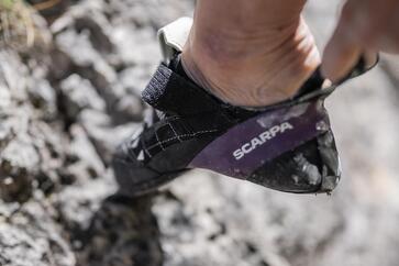 Close-up of a foot wearing a climbing shoe on rocky terrain.