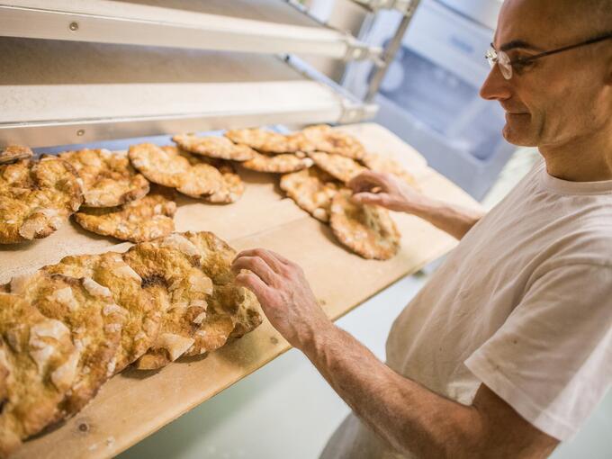 A man is standing in a bakery and checking freshly baked Schüttelbrot on a shelf