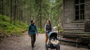 A man and a woman are walking through the forest with a stroller