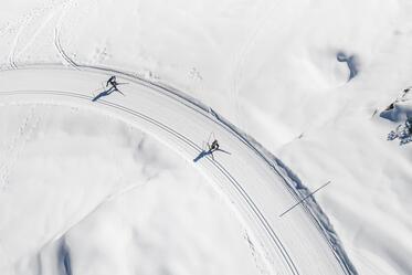 Aerial view of a snow-covered bend with tracks in the snow and two people on a winter trail.