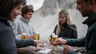 A group of people is sitting at a table in the Sexten Dolomites, drinking beer and playing cards