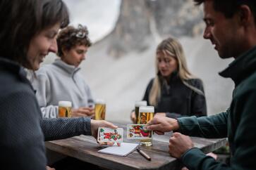 A group of people is sitting at a table in the Sexten Dolomites, drinking beer and playing cards