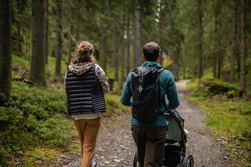 Un uomo e una donna passeggiano nel bosco con un passeggino
