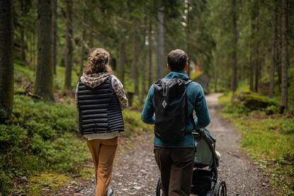 A man and a woman are walking through the forest with a stroller