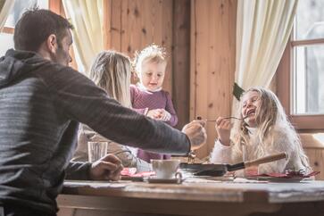 Una famiglia con due bambini è seduta a un tavolo e gusta piatti altoatesini